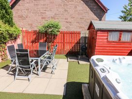 A patio with a black glass table and six chairs next to a red wooden shed and a hot tub at Smiddy Bothy in Edzell