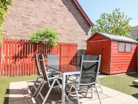 An outdoor patio with a glass table and six chairs near a red wooden shed and a red fence at Smiddy Bothy in Edzell