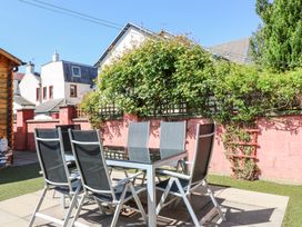 An outdoor patio with a glass table and six chairs surrounded by a red brick wall and greenery at Smiddy Bothy in Edzell