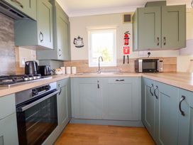 A kitchen with green cabinets a gas stove oven microwave kettle toaster sink and countertop at Lodge 9- Lamorna Tregolds near St Merryn