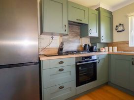 A kitchen with green cabinets a stainless steel refrigerator a gas stove an oven a kettle a toaster and containers on the countertop at Lodge 9- Lamorna Tregolds near St Merryn