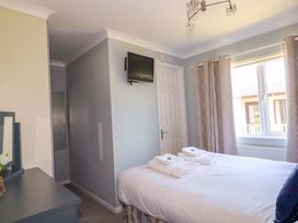 A bedroom with a bed with folded towels a wall-mounted TV a window with curtains and a dresser with a mirror at Lodge 9- Lamorna in Tregolds near St Merryn