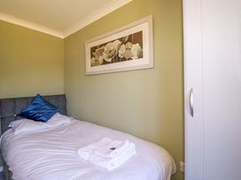 A bedroom with a single bed with white linens and blue pillow a white wardrobe and a floral painting on the wall at Lodge 9- Lamorna in Tregolds near St Merryn