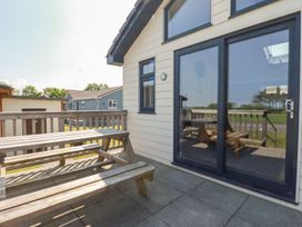 An outdoor patio with a wooden picnic table and benches next to a building with glass sliding doors and a window at Lodge 18 in St Merryn