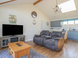 A living area with a grey recliner sofa wooden coffee table television on a stand and a kitchen with blue cabinets at Lodge 18 in St Merryn