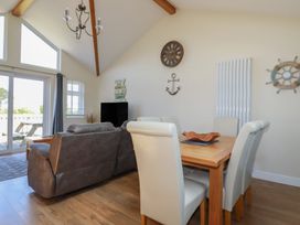 A dining table with six chairs and a living room with a sofa near glass doors at Lodge 18 in St Merryn
