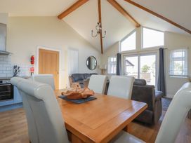 A dining area with a wooden table and leather chairs next to a living room with sofas and large windows at Lodge 18 in St Merryn