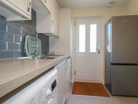 A kitchen with a washing machine under the counter a stainless steel sink a drying rack a refrigerator and a white door with windows at Lodge 18 in St Merryn