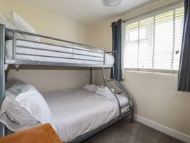 A bedroom with a metal bunk bed and window with blinds and curtains at Lodge 18 in St Merryn