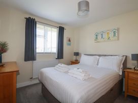 A bedroom with a double bed with white linens two bedside tables with lamps a window with dark curtains and beach themed pictures at Lodge 18 in St Merryn