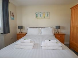 A bedroom with a bed with white linens and stacked towels on top two wooden bedside tables with lamps and a wooden wardrobe at Lodge 18 in St Merryn