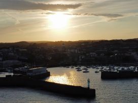 A sunset over a harbor with boats and a lighthouse at Tide Watch in Penzance