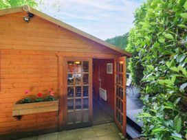 A wooden cabin with a door and flowers in a planter at Stumps Cross Lodge Upper Coscombe near Winchcombe