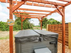 An outdoor hot tub under a wooden pergola with string lights at Woodpecker in Lode near Bottisham