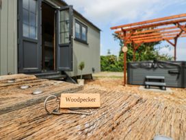 A wooden key tag with the word Woodpecker on a table outside a building with open doors and a hot tub under a wooden pergola in a garden at Woodpecker in Lode near Bottisham