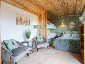 A bedroom with bunk beds double bed armchairs and a wooden ceiling at Woodpecker in Lode near Bottisham
