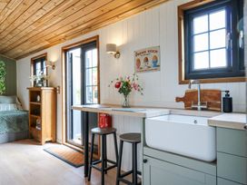 A kitchen area with a sink stools a table flowers on the table and a cupboard next to a door at Woodpecker in Lode near Bottisham