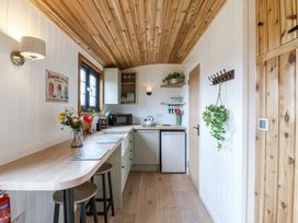 A small kitchen with wooden ceiling and countertops stools a sink microwave and a mini fridge at Woodpecker in Lode near Bottisham