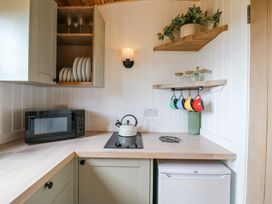 A kitchen corner with a microwave oven, kettle, hanging cups, shelves with glasses and a potted plant at Woodpecker in Lode near Bottisham