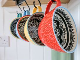 Six colorful ceramic mugs with black and white patterns hanging on hooks in a kitchen at Woodpecker in Lode near Bottisham