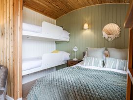A bedroom with a double bed and white bunk beds with pillows a nightstand lamp and a round mirror on the wall at Woodpecker in Lode near Bottisham