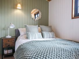 A bedroom with a bed covered with pillows and a textured blanket next to a wooden nightstand at Woodpecker in Lode near Bottisham
