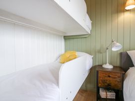 A bunk bed with white bedding and a yellow pillow next to a wooden nightstand with a lamp and books at Woodpecker in Lode near Bottisham