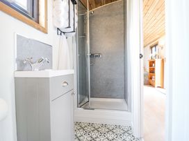 A bathroom with a shower enclosure a sink cabinet and towels with a view into a bedroom at Woodpecker in Lode near Bottisham