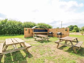 An outdoor area with wooden picnic tables grills and a wooden fence at Woodpecker in Lode near Bottisham