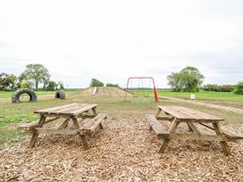 An outdoor playground with two wooden picnic tables a red swing set large tires and a dirt mound with a slide at Woodpecker in Lode near Bottisham