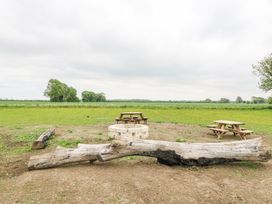 An outdoor fire pit with stone surrounds and wooden benches in a grassy field at Woodpecker in Lode near Bottisham