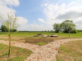 An outdoor area with wood chip paths, newly planted trees, picnic benches, logs, and a stone fire pit at Woodpecker in Lode near Bottisham
