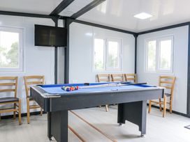 A game room with a pool table chairs and a wall-mounted television at Woodpecker in Lode near Bottisham