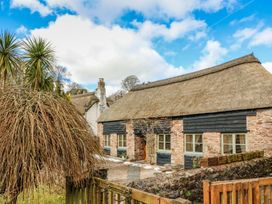 A stone cottage with thatched roof and wooden shutters surrounded by trees and a wooden fence at Meadow Thatch in Cockington