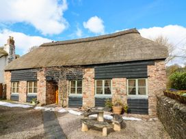 Stone and wood cottage with thatched roof and outdoor stone table and benches at Meadow Thatch in Cockington