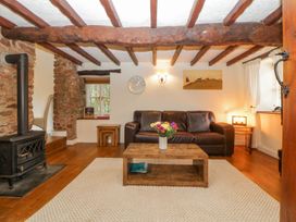 A living room with wooden beams on the ceiling a wood stove and a leather sofa at Meadow Thatch in Cockington