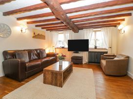 A living room with exposed wooden ceiling beams a leather sofa a fabric armchair a wooden coffee table a flat screen TV and windows with white curtains at Meadow Thatch in Cockington