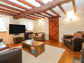 A living room with wooden beams on the ceiling a wooden coffee table with flowers leather chairs and a wooden door at Meadow Thatch in Cockington