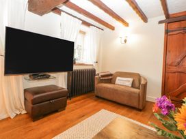 A small living room with a brown sofa and a large mounted TV at Meadow Thatch in Cockington