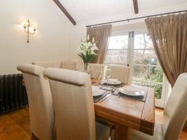 A dining room with a wooden table set with plates utensils and glasses surrounded by cream chairs and a window with brown curtains at Meadow Thatch in Cockington