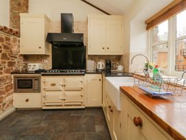 A kitchen with cream cabinets stone wall a farmhouse sink and a black stove at Meadow Thatch in Cockington