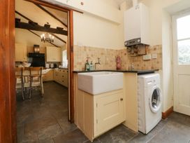 A kitchen with a washing machine and sink next to a door leading to a dining area with wooden table and chairs at Meadow Thatch in Cockington