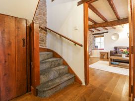 A carpeted staircase next to a wooden door leading to a living room with wooden beams on the ceiling and a sofa at Meadow Thatch in Cockington