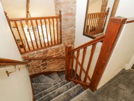 A carpeted staircase with wooden banisters and stone wall section at Meadow Thatch in Cockington