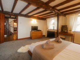 A bedroom with a wooden bed and folded towels on it a dresser with a TV two windows with white curtains and a wooden desk with a mirror at Meadow Thatch in Cockington