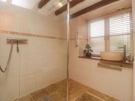 A shower area with tiled walls and floor with a faucet and a small bonsai plant on the window sill at Meadow Thatch in Cockington