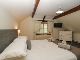 A bedroom with a bed towel rolls a dresser a window with curtains and a wall-mounted television at Meadow Thatch in Cockington