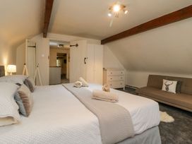 A bedroom with a double bed towels on the bed a sofa with a pillow a chest of drawers and a full-length mirror at Meadow Thatch in Cockington