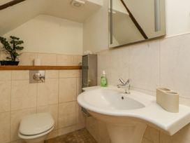 A bathroom with a white toilet, a white sink with a faucet, a soap dispenser, a toothbrush holder, a wall-mounted mirror, a small potted plant, and beige tiled walls at Meadow Thatch in Cockington