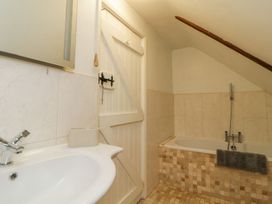 A bathroom with a sink, a white wooden door, and a bathtub with a gray towel on the edge at Meadow Thatch in Cockington